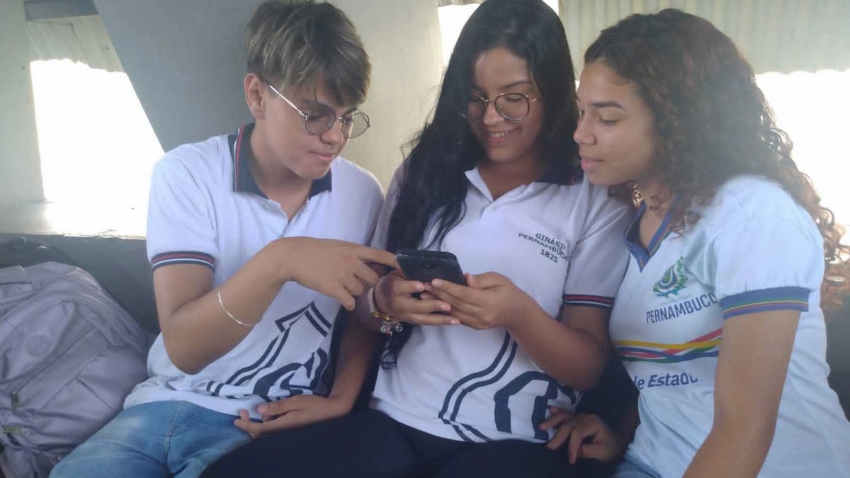 three girls sitting on a couch looking at a cell phone